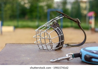 An iron metal muzzle for a large dog with a leather belt on the background of a dog walking and training area. Safety and education of the dog. Accessories for dogs - Shutterstock ID 1981574162