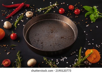 Iron plate stands on a dark background with mushrooms, peppercorns, red chili peppers, salt, tomatoes and basil on a black background - Powered by Shutterstock