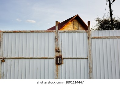 Iron Rusty Fence. White Corrugated Metal Or Zinc Texture Surface Or Galvanize Steel In The Vertical Line Background. The Roof Of The House Against The Sky