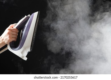 An iron with a steam generator sprays white hot steam on a black background. Steaming clothes, ironing