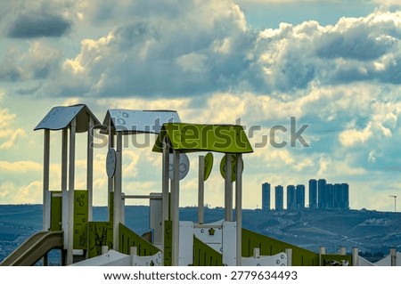 An ironic composition created by the interplay between the roofs of the slides at the playground up ahead and the skyscrapers visible on the horizon.