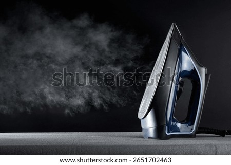 Ironing concept with steaming iron and stack of ironed and folded white shirts on black table and dark background. Front view.