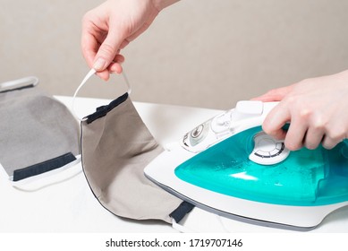 Ironing A Reusable Cloth Face Mask For Protection From COVID-19, Epidemic, Pandemic. Thermal Disinfection Cotton Homemade Masks After Washing In Washing Machine.