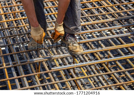 Ironworker securing steel rebar framing with wire plier cutter tool at construction site. Install rebar in the footing.
