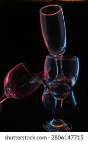 An irregular, artistic stack of glasses featuring a champagne flute balanced precariously on top, glowing with neon outlines.