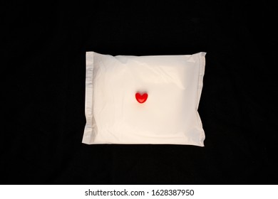 Irregular Period Concept. Menstrual Cycle Pad With Red Hearts On Black Background. Menorrhagia Or Heavy Menstruation Bleeding. Feminine Critical Days Hygiene Products. Creative Minimalism Dark Photo