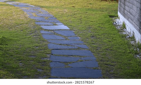 Irregular Stepping Stone Path Winding Through Green Grass Lawn Towards a Building Wall