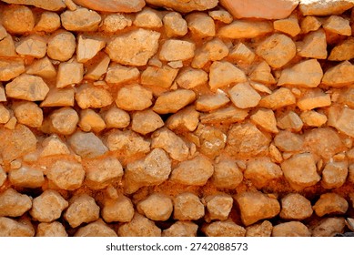 Irregular Stone Wall Texture

A close‑up view of a stone wall constructed with irregularly shaped rocks tightly packed together. The stones vary in size and form, with reddish‑brown mortar filling the gaps, creating a rugged and uneven surface. The coloration suggests natural, locally sourced materials, highlighting traditional rustic construction methods. This image emphasizes raw texture and detail, making it suitable for studies in geology, architecture, or cultural heritage preservation. 
Scientific name: Lithic material