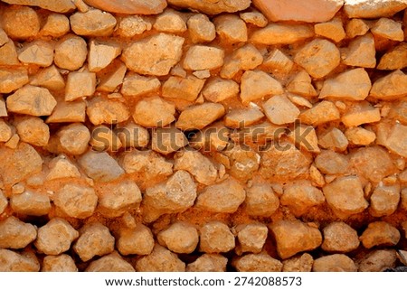 Irregular Stone Wall Texture

A close‑up view of a stone wall constructed with irregularly shaped rocks tightly packed together. The stones vary in size and form, with reddish‑brown mortar filling the gaps, creating a rugged and uneven surface. The coloration suggests natural, locally sourced materials, highlighting traditional rustic construction methods. This image emphasizes raw texture and detail, making it suitable for studies in geology, architecture, or cultural heritage preservation. 
Scientific name: Lithic material