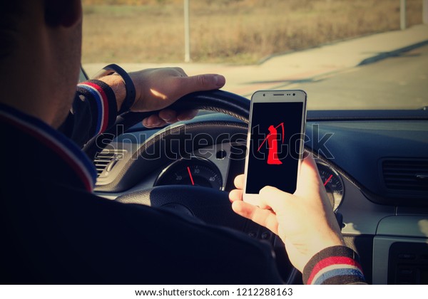 An irresponsible man driving a car with a mobile\
phone in his hand.A man holds a driving wheel and a mobile phone\
with symbol Grim Reaper.