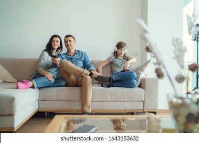 Irresponsible Parents Ignoring Lonely Daughter. Bored Young Girl Using Laptop On Bed While Mom And Dad Watching TV And Not Paying Attention To Her