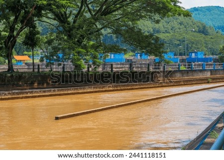 Irrigation canal that flows water from the Serayu River and passes through the weir to the rice fields in Kebasen, Banyumas, Indonesia. Lush trees provide the backdrop for this brown water.