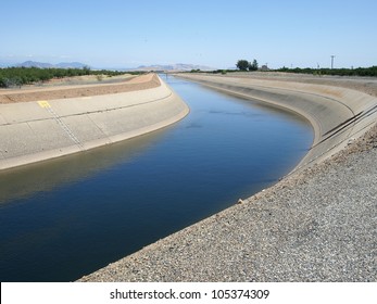 Irrigation water flows in a canal near an orange grove.