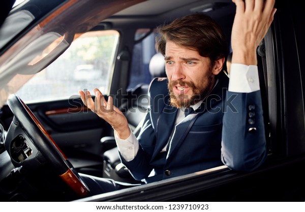 irritable man in a suit sits behind the wheel of a\
car                           \
