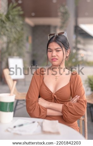 An irritated asian woman crosses her arms as she is disgusted with the news she just heard. A lady despising someone. Outdoor cafe scene.