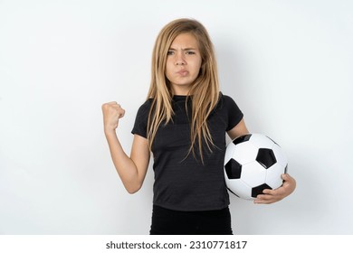 Irritated beautiful caucasian teen girl wearing sportswear holding a football ball over white wall blows cheeks with anger and raises clenched fists expresses rage and aggressive emotions. Furious mod - Shutterstock ID 2310771817