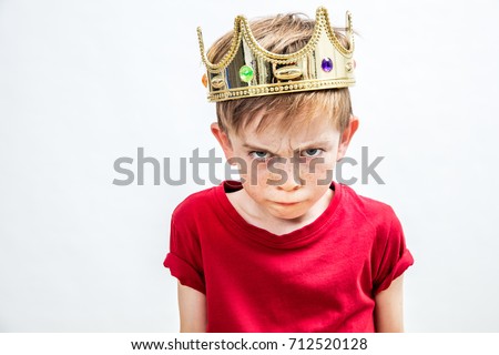irritated beautiful spoiled boy with frowning freckles and a dirty look wearing a golden crown for mad attitude facing parenthood and education, white background, indoors
