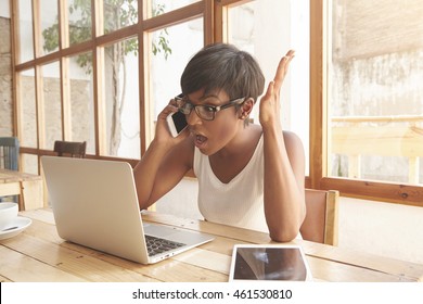 Irritated Brown-skinned Woman Is Talking With Business Partners On Phone About Her Work Project. Young Female Boss Is Totally Upset With News And Holding Her Hand In Indignity. Sideways Portrait.