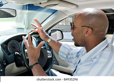 An Irritated Business Man Driving A Car Is Expressing His Road Rage With His Hands In The Air.