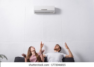irritated couple suffering from heat at home with broken air conditioner