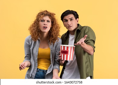 Irritated Couple Watching Bad Movie With Bucket Of Popcorn, Isolated On Yellow