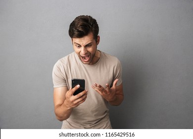 Irritated guy 20s in t-shirt screaming in anger while looking at smartphone isolated over gray background - Powered by Shutterstock