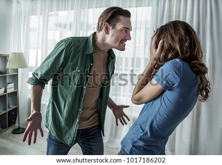Irritated husband is shouting at his wife with violence. Woman is covering her face with fear