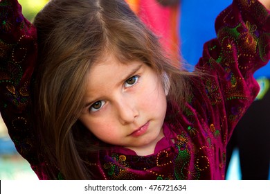 An Irritated Little Girl Gives An Intense Look.  She Has Her Arms Up And Is Leaning On Something With Her Head Cocked To The Side, Looking At The Viewer With A Furrowed Brow And Intense Eyes.