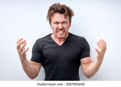 Irritated man wearing black t-shirt standing over isolated white background crazy and mad shouting and yelling with aggressive expression and arms raised. Frustration concept. Human emotions - Shutterstock ID 2007903698