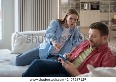 Irritated nervous jealous woman shouts at husband accusing of cheating and betrayal pointing finger at cellphone. Secretive man ignores worried distrustful wife. Misunderstanding discord resentment