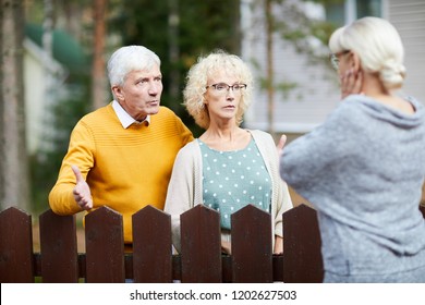 Irritated Senior Couple Discussing Trouble With Their Neighbour Behind Wooden Fence