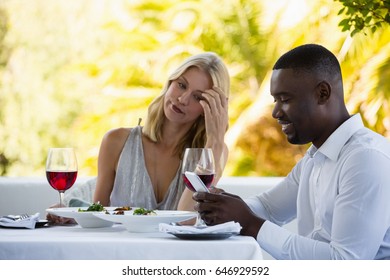 Irritated woman looking at man using phone at table in restaurant - Powered by Shutterstock