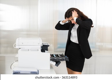 Irritated young businesswoman looking at printer machine at office