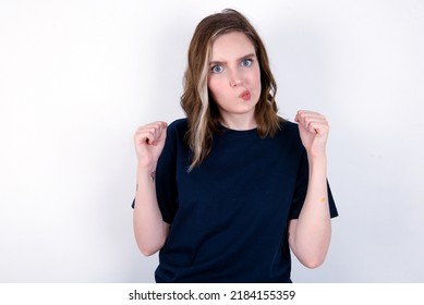 Irritated young caucasian woman wearing black T-shirt over white background blows cheeks with anger and raises clenched fists expresses rage and aggressive emotions. Furious model - Shutterstock ID 2184155359