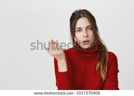 Irritated young female with dark hair in ponytail has displeased face expression, gestures actively, expresses negativeness, isolated against gray background. Girl asking so what, who cares