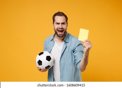 Irritated young man in casual blue shirt posing isolated on yellow orange wall background. People lifestyle concept. Mock up copy space. Hold soccer ball, yellow card propose player retire from field - Shutterstock ID 1608609415