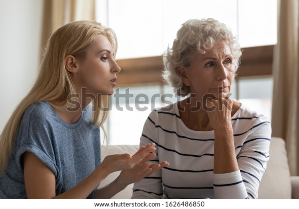 Irritated young woman asserting opinion to\
offended middle aged mother at home. Annoyed blonde grown up\
daughter arguing with stubborn mature elderly mom, two generations\
family disagreements\
concept.