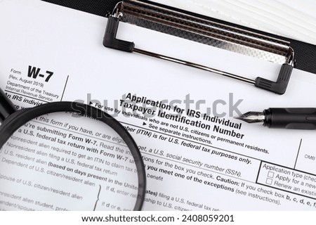 IRS Form W-7 Application for IRS Individual taxpayer identification number, blank on A4 tablet lies on office table with pen and magnifying glass close up