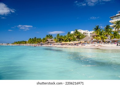 ISLA MUJERES ISLAND, MEXICO - APR 2022: People Sunbathing On The White Sand Beach With Umbrellas, Bungalow Bar And Cocos Palms, Turquoise Caribbean Sea, Isla Mujeres Island, Caribbean Sea, Cancun.