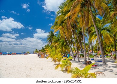 ISLA MUJERES ISLAND, MEXICO - APR 2022: People Are Sunbathing In The Shadow Of Cocos Palms On White Sand Beach, Isla Mujeres Island, Caribbean Sea, Cancun, Yucatan, Mexico.