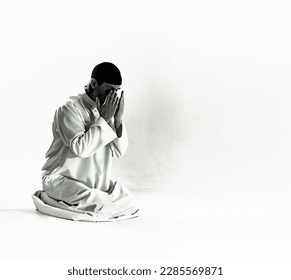 Islam religious concept.Muslim man in traditional clothing kneels on prayer mat, holds palms in front of face and performs Salah, ritual prayer of Islam. devotion, piety, and spiritual aspect of