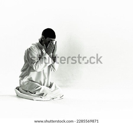 Islam religious concept.Muslim man in traditional clothing kneels on prayer mat, holds palms in front of face and performs Salah, ritual prayer of Islam. devotion, piety, and spiritual aspect of
