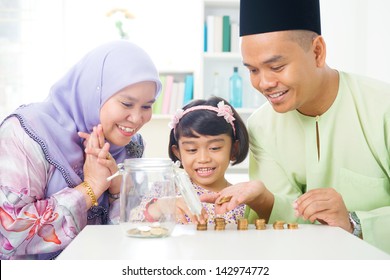 Islamic Banking Concept. Southeast Asian Family Counting Money At Home. Little Malay Girl And Parents Saving Money. Muslim Father, Mother And Daughter Living Lifestyle.