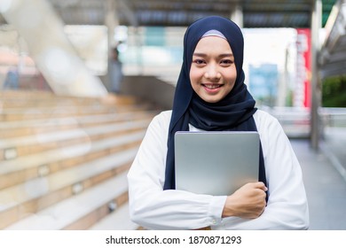 Islamic Student Or Working Woman Standing With Her Arms Crossed Holding Her Laptop, Smiling Confidently.