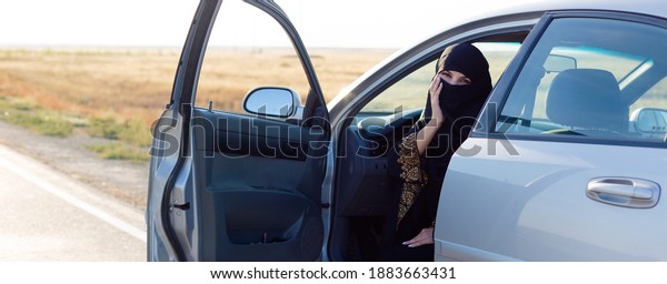 Islamic woman sitting in car with the front door\
wide open.