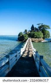 Island Oasis: Experience the Tranquility of a Small Bridge Connecting to a Tropical Paradise, with a Serene Temple Amidst the Scenic Beauty of Balekambang Beach, Embraced by a Bright Blue Sky and Refr