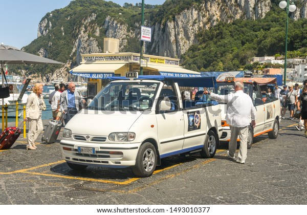 ISLE OF CAPRI, ITALY - AUGUST 2019: People with\
luggage at the taxi rank in the port on the Isle of Capri after\
arriving on a ferry.
