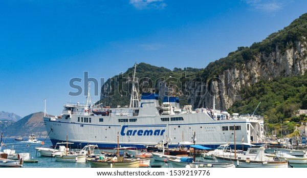 ISLE OF CAPRI, ITALY - AUGUST 2019: Large car\
ferry operated by Caremar docked amongst small fishing boats in the\
port on the Isle of Capri.
