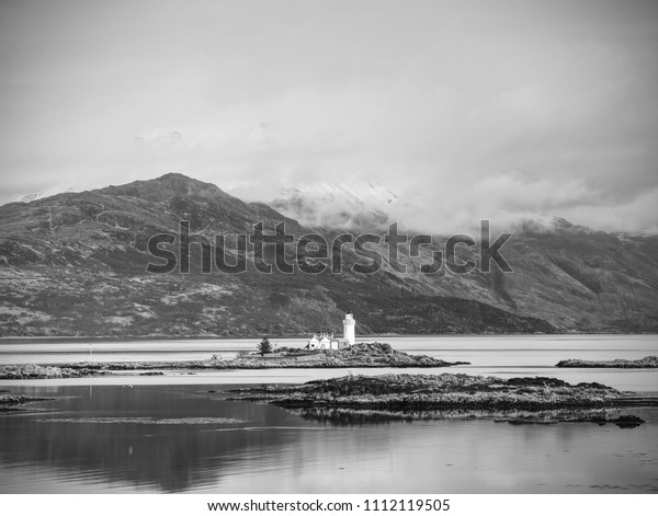 Isle\
Ornsay with white tower of Lighthouse; Isle of Skye; Scotland.\
Sunny winter day with snowy mountains in\
background.