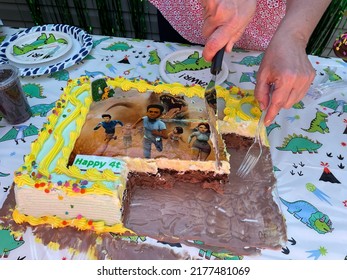 Islip Terrace, NY, USA, 6.26.22 - The Top Down, Close Up View Of A Jurassic World Birthday Cake That Is Being Sliced And Served On Dinosaur Cake Plates. The Ice Cream Cake Is Melting.